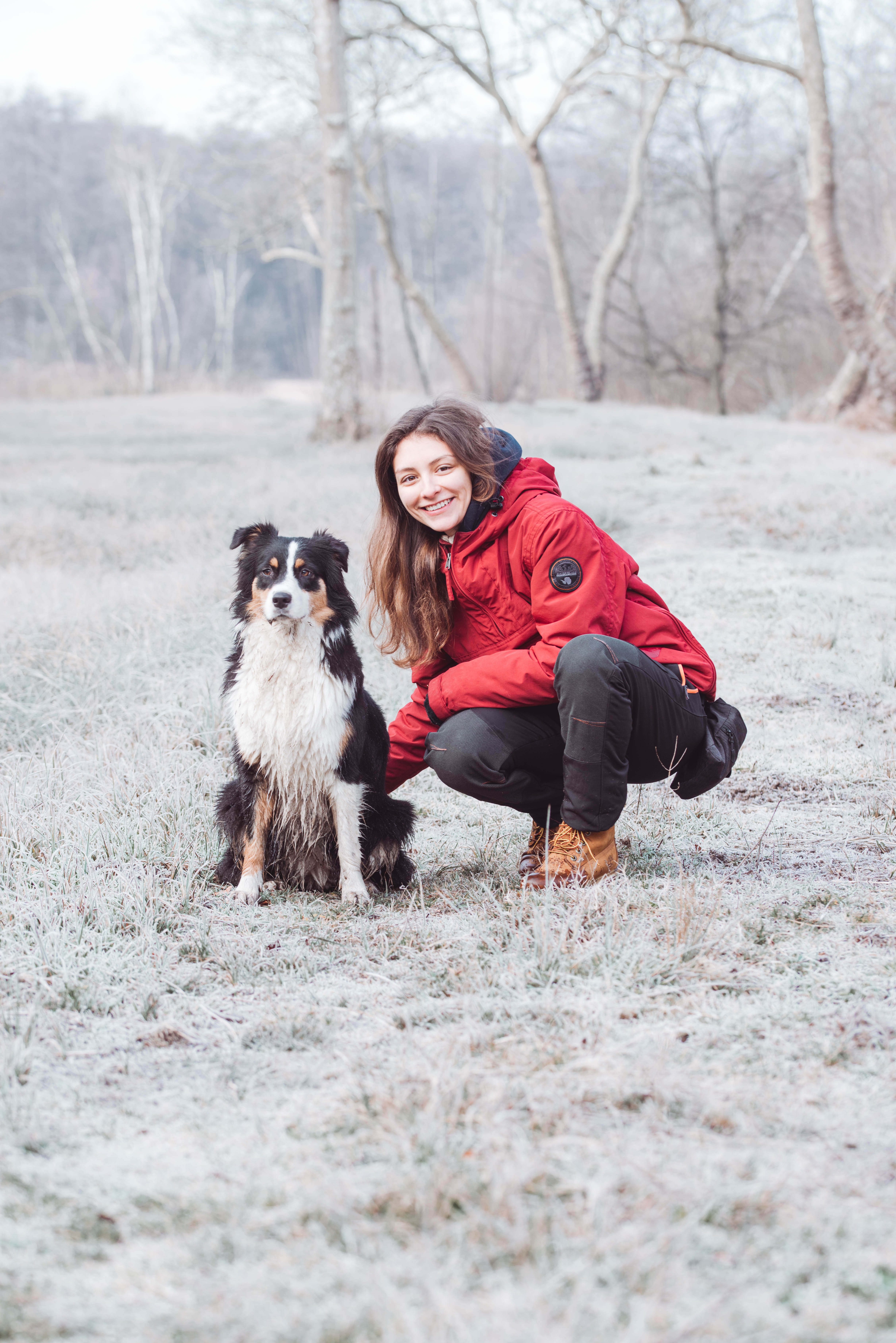 Floriane, éducatrice canine Eden K9, accroupie aux côtés de son chien dans un champ givré en hiver